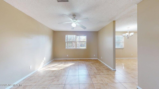 spare room featuring ceiling fan with notable chandelier, a wealth of natural light, baseboards, and light tile patterned floors