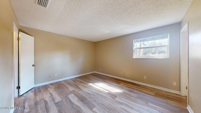 empty room with visible vents, a textured ceiling, baseboards, and wood finished floors