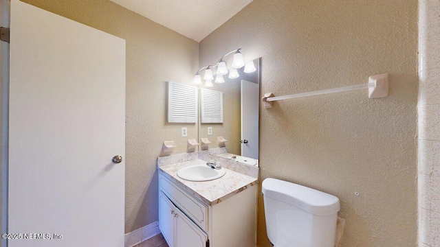 bathroom with toilet, vanity, and a textured wall