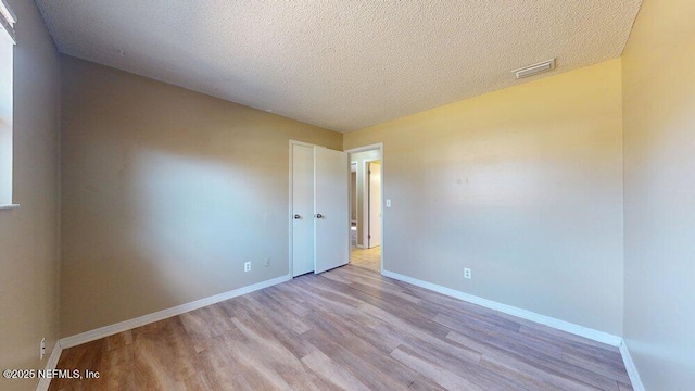 spare room featuring a textured ceiling, wood finished floors, visible vents, and baseboards