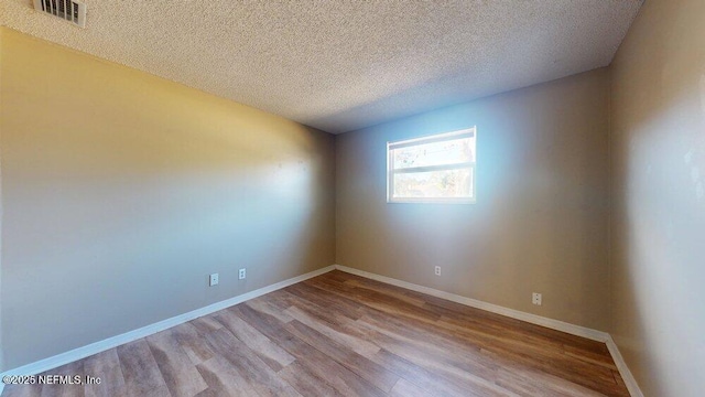 empty room featuring baseboards, a textured ceiling, visible vents, and wood finished floors