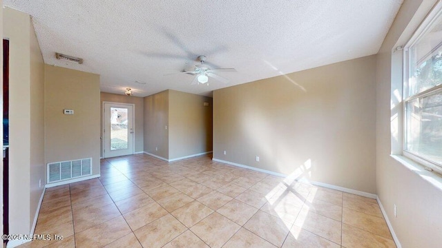 empty room with light tile patterned floors, plenty of natural light, visible vents, and ceiling fan