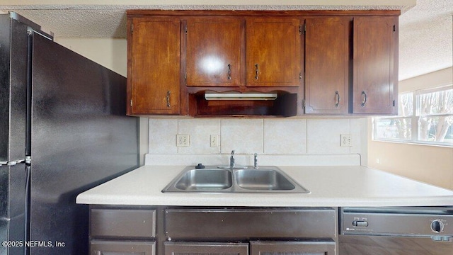 kitchen with dishwasher, light countertops, a sink, and freestanding refrigerator