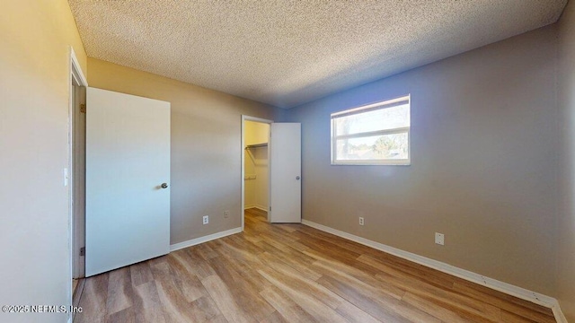 unfurnished bedroom with baseboards, wood finished floors, a walk in closet, a textured ceiling, and a closet