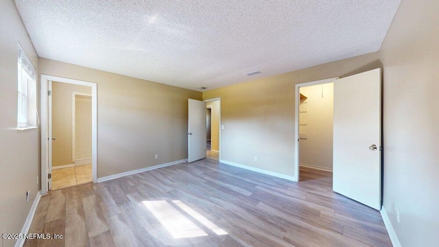 unfurnished bedroom featuring light wood-style floors, a spacious closet, baseboards, and a textured ceiling