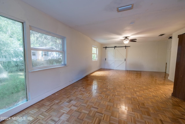 spare room featuring a barn door, ceiling fan, and light parquet flooring