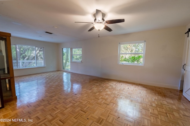 spare room with a barn door, light parquet floors, a wealth of natural light, and ceiling fan