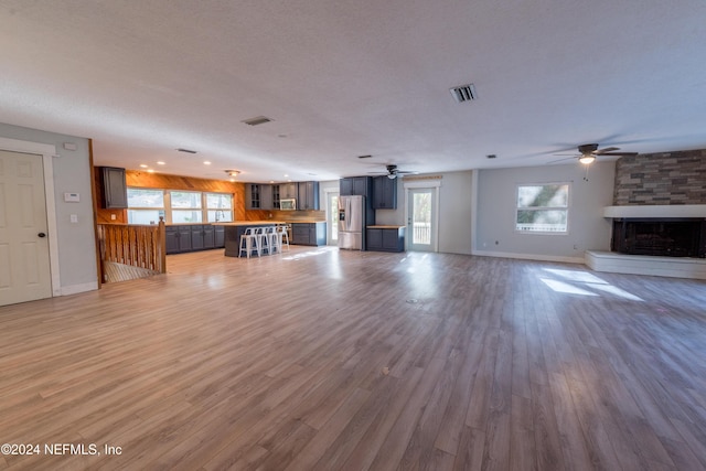 unfurnished living room featuring a stone fireplace, a wealth of natural light, a textured ceiling, and hardwood / wood-style flooring