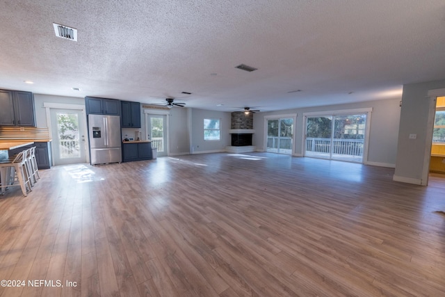 unfurnished living room featuring a fireplace, wood-type flooring, a textured ceiling, and ceiling fan