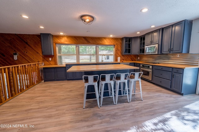 kitchen with light hardwood / wood-style flooring, butcher block countertops, wood walls, a kitchen bar, and appliances with stainless steel finishes