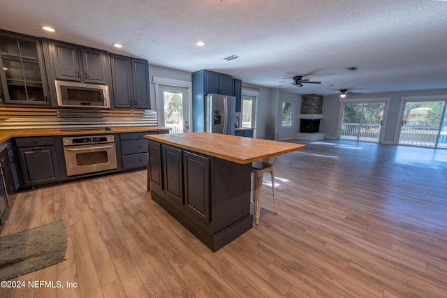 kitchen featuring wood counters, a stone fireplace, appliances with stainless steel finishes, light hardwood / wood-style floors, and a kitchen bar