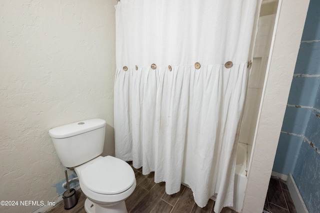 bathroom with hardwood / wood-style floors, shower / bathtub combination with curtain, and toilet