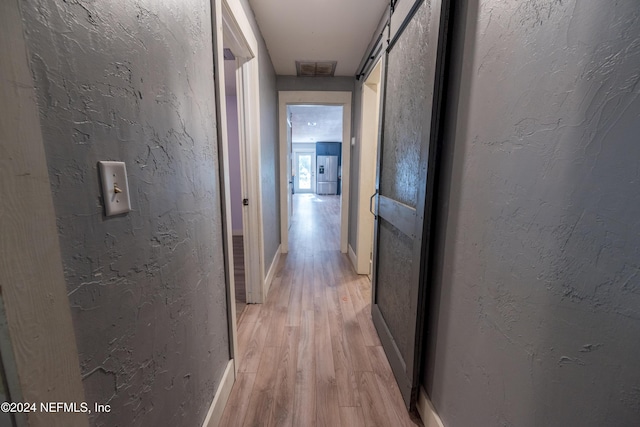 hallway with a barn door and light hardwood / wood-style floors