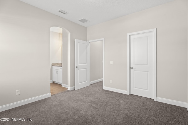 unfurnished bedroom with a textured ceiling, light carpet, and connected bathroom