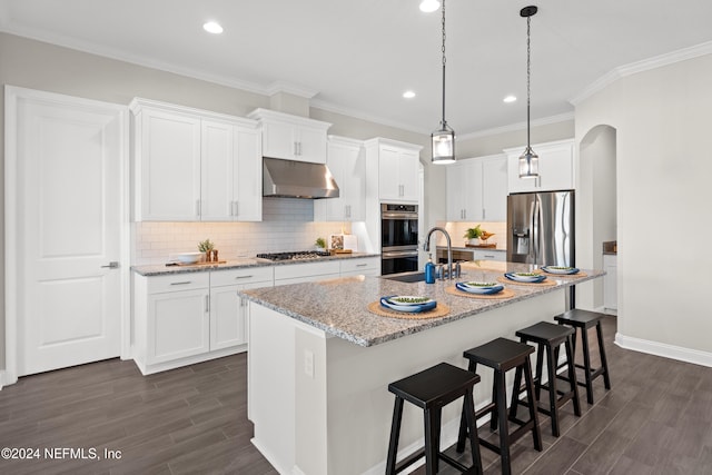 kitchen featuring dark hardwood / wood-style flooring, light stone counters, stainless steel appliances, white cabinets, and an island with sink