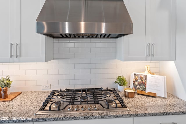 kitchen with white cabinetry, wall chimney range hood, tasteful backsplash, light stone counters, and stainless steel gas stovetop