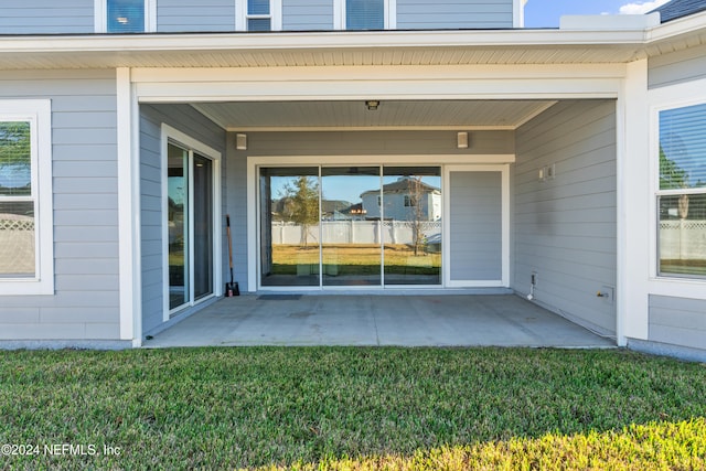 view of exterior entry featuring a lawn and a patio