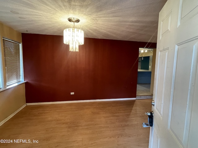 empty room with hardwood / wood-style floors, a textured ceiling, and a notable chandelier