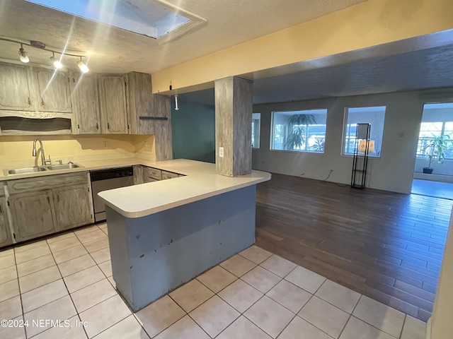 kitchen featuring dishwasher, sink, a skylight, light hardwood / wood-style flooring, and kitchen peninsula