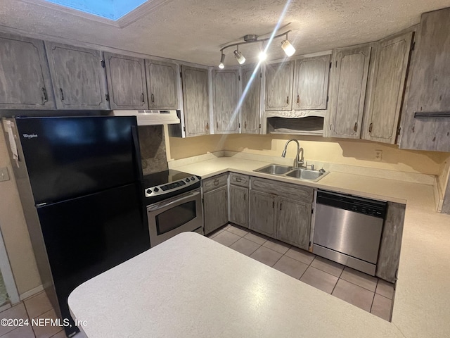 kitchen with a skylight, sink, a textured ceiling, light tile patterned flooring, and appliances with stainless steel finishes