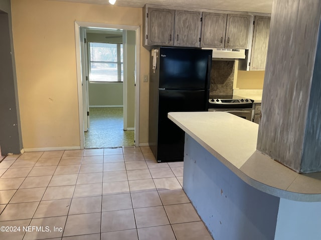 kitchen featuring tasteful backsplash, black refrigerator, light tile patterned flooring, and stainless steel electric range