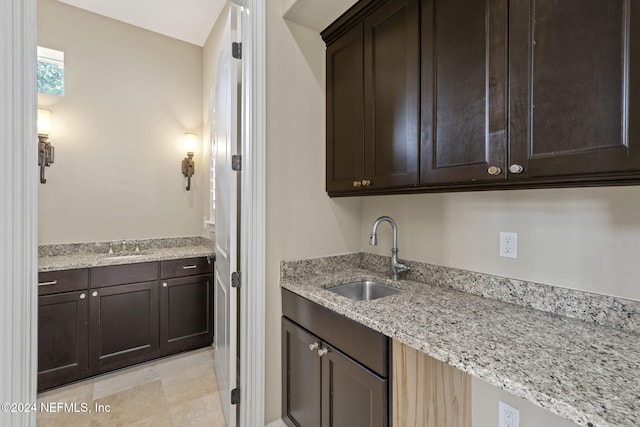 kitchen with light stone counters, dark brown cabinetry, and sink