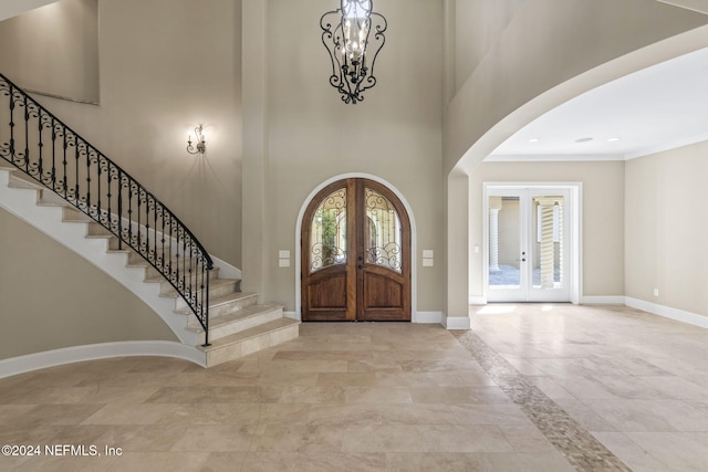 foyer featuring a chandelier, a towering ceiling, crown molding, and french doors