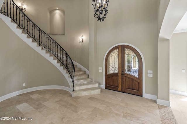 foyer entrance with crown molding, french doors, a high ceiling, and a notable chandelier