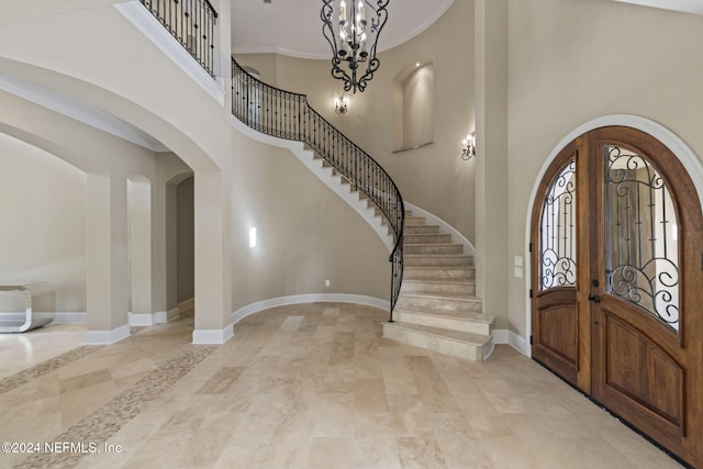 entryway featuring a notable chandelier, a towering ceiling, crown molding, and french doors