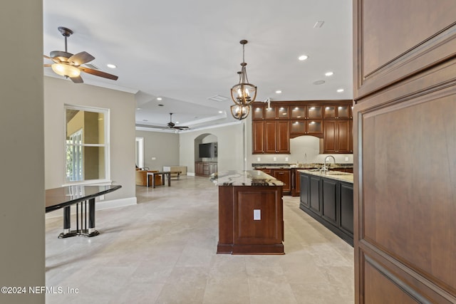 kitchen with a center island, ceiling fan with notable chandelier, sink, decorative light fixtures, and light stone counters