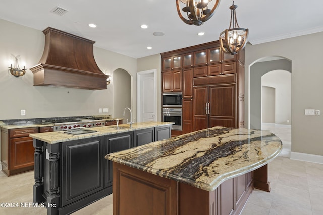 kitchen with sink, premium range hood, built in appliances, a chandelier, and a kitchen island with sink