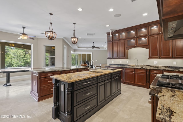 kitchen featuring dark brown cabinets, ceiling fan with notable chandelier, a kitchen island with sink, sink, and decorative light fixtures