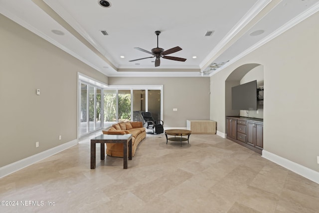 living room with a raised ceiling, ceiling fan, and crown molding