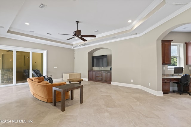 living room with a tray ceiling, crown molding, ceiling fan, and built in desk