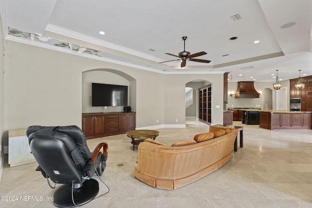 living room featuring a raised ceiling, ceiling fan, crown molding, and sink