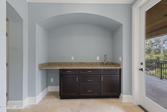 bar featuring dark brown cabinetry, light stone countertops, sink, and light tile patterned floors