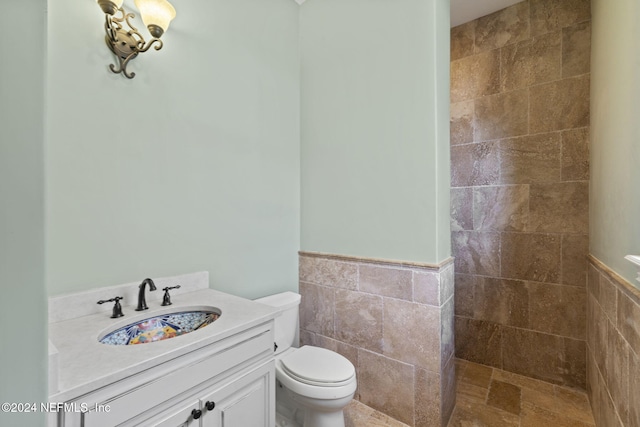 bathroom with tiled shower, vanity, toilet, and tile walls