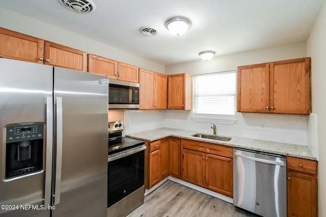 kitchen featuring light stone countertops, sink, tasteful backsplash, light hardwood / wood-style flooring, and appliances with stainless steel finishes