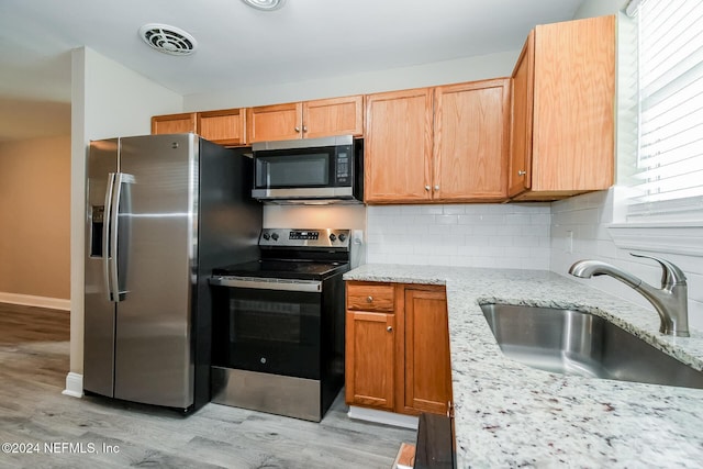 kitchen featuring light stone counters, sink, stainless steel appliances, and light hardwood / wood-style flooring