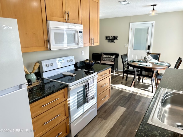 kitchen featuring white appliances, dark wood-type flooring, dark stone countertops, a textured ceiling, and sink