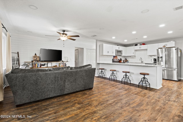 living room with ceiling fan, sink, wood walls, and dark hardwood / wood-style floors