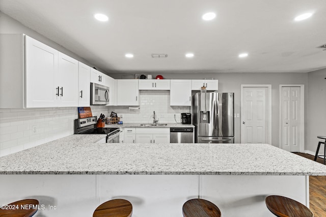 kitchen with a kitchen bar, wood-type flooring, stainless steel appliances, and white cabinetry