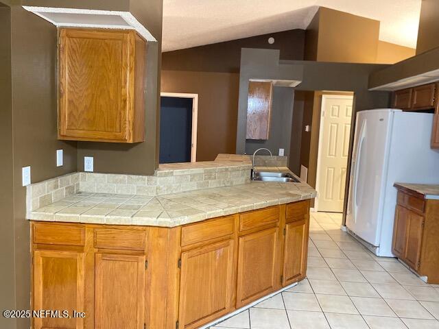 kitchen featuring light tile patterned flooring, sink, vaulted ceiling, tile counters, and white fridge