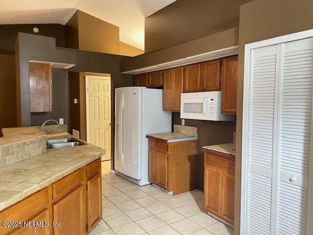 kitchen featuring light tile patterned flooring, tile countertops, lofted ceiling, sink, and white appliances