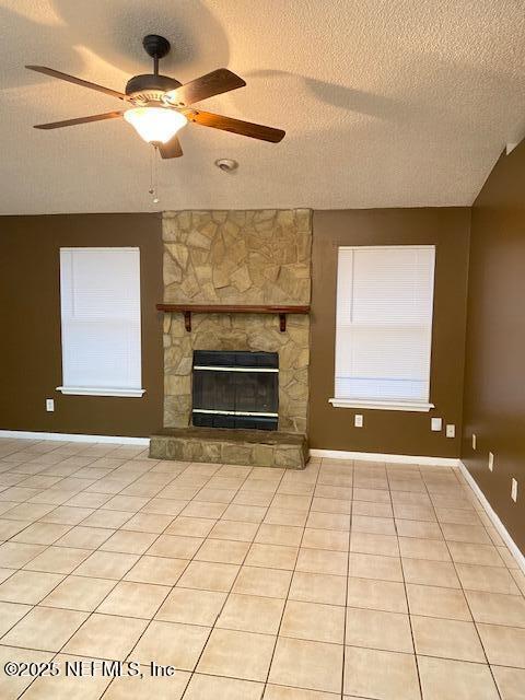 unfurnished living room featuring light tile patterned flooring, ceiling fan, a fireplace, and a textured ceiling