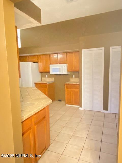 kitchen with light tile patterned floors, tile counters, and white appliances