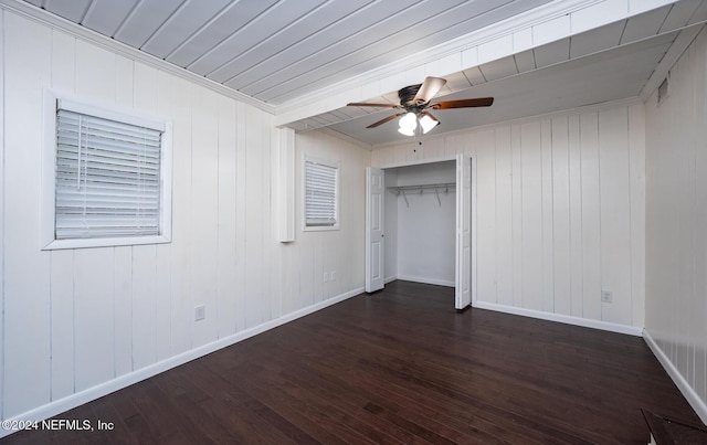 unfurnished bedroom featuring dark wood-type flooring, crown molding, wooden walls, ceiling fan, and a closet