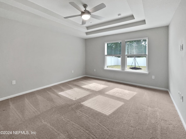 carpeted empty room with a raised ceiling and ceiling fan