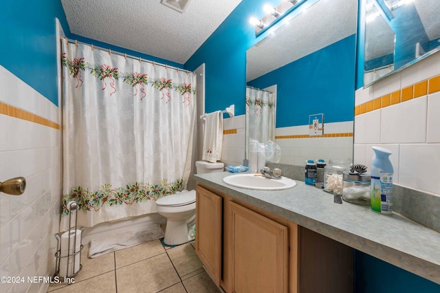 full bathroom with tile patterned floors, vanity, a textured ceiling, tile walls, and toilet