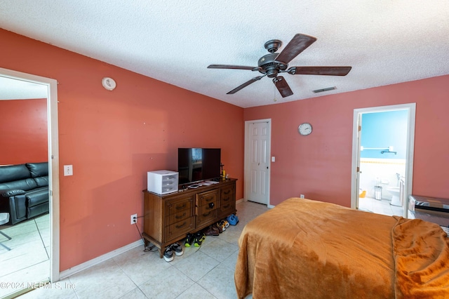 bedroom featuring ceiling fan, ensuite bathroom, light tile patterned floors, and a textured ceiling